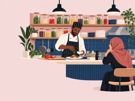A cook plates a dish at an open counter in full view of a seated diner, ingredients on open shelves behind.